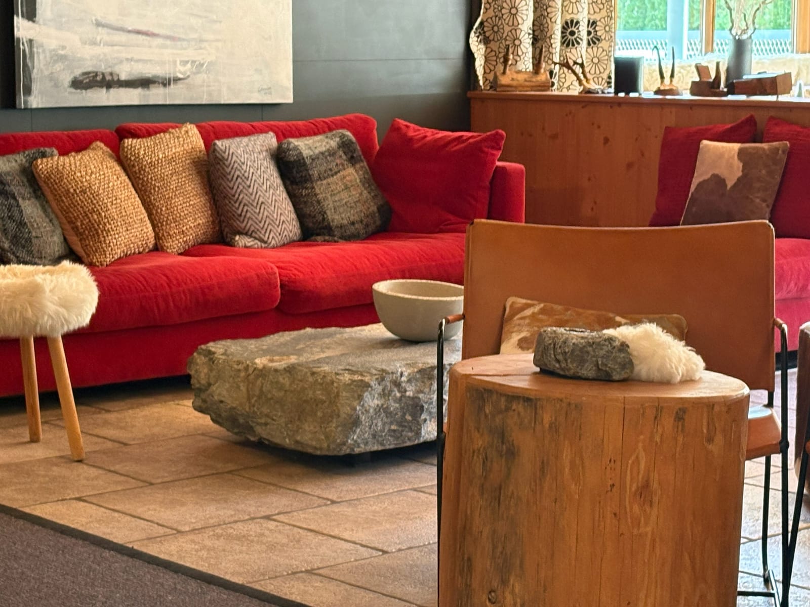 Rotes Sofa mit Kissen, Baumstamm-Beistelltische und Steinhocker – MONTAFONLodge