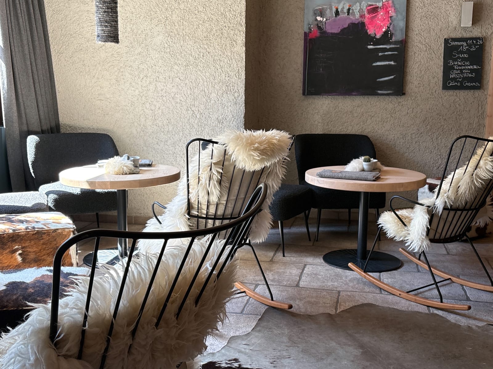 Lounge mit schwarzen Korbsesseln mit Schaffellen und runden Tischen – MONTAFONLodge