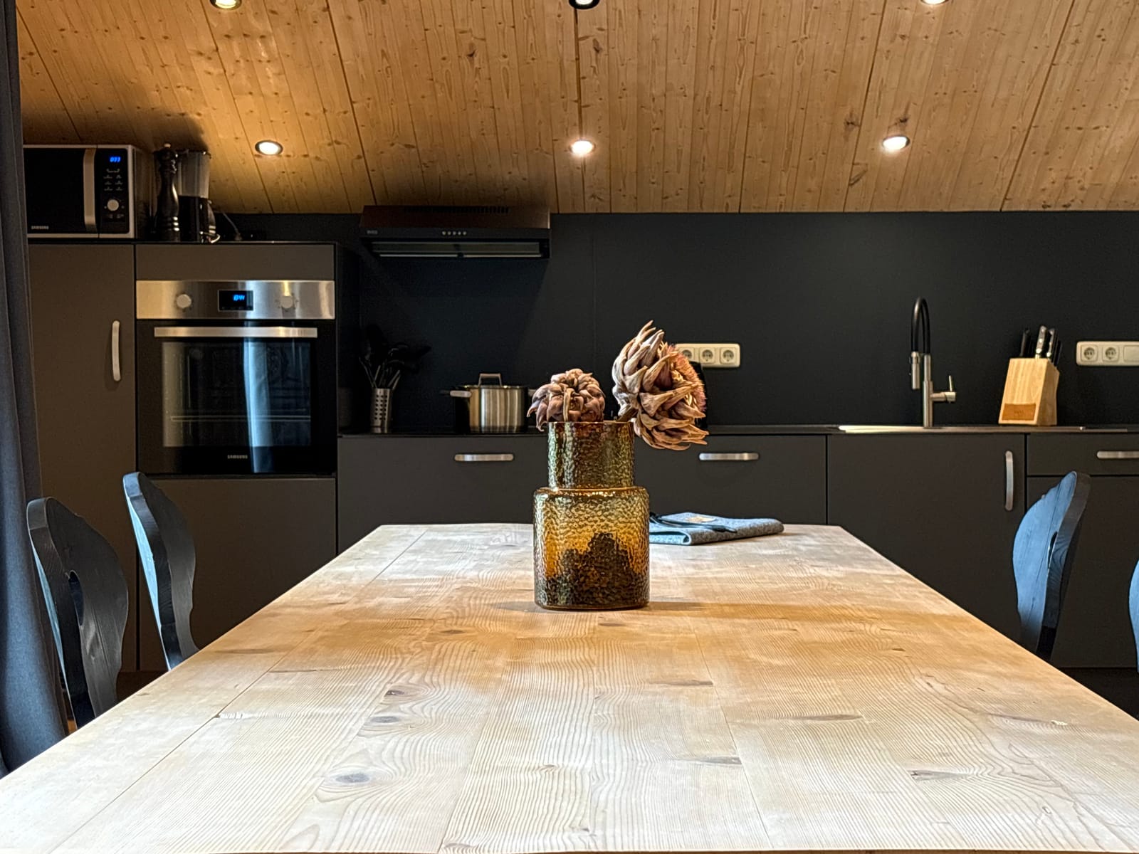 Essplatz mit Holztisch, Deko-Blumen und offener Küche – MONTAFONLodge