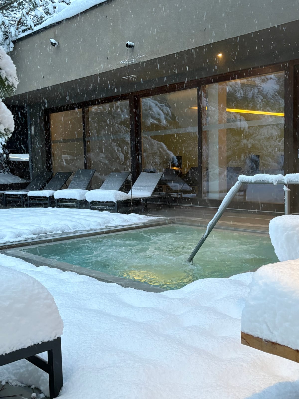 Außenpool im Schnee mit Liegen hinter Glasfront – MONTAFONLodge