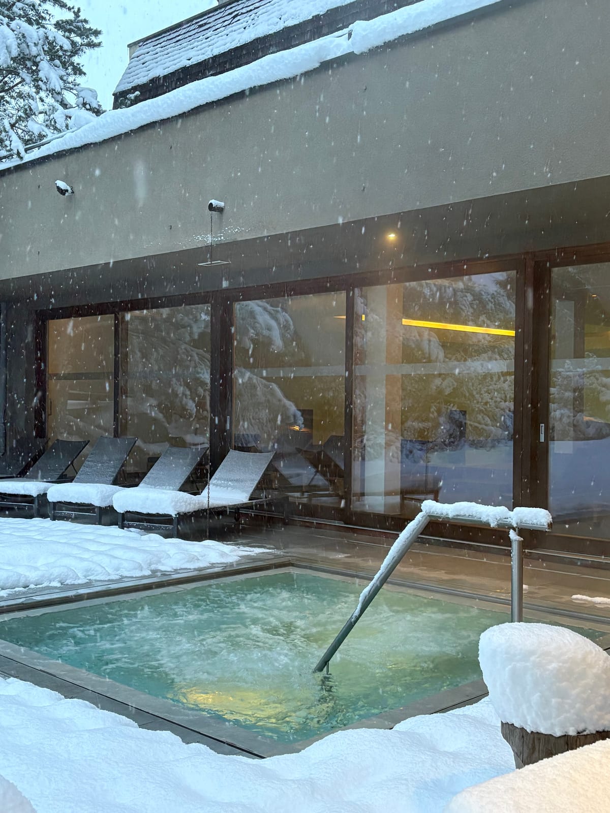 Außenpool im Schnee, Ruheliegen innen hinter Glasfront – MONTAFONLodge