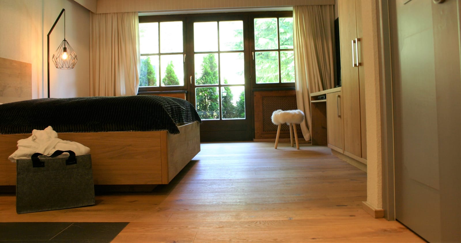 Doppelbett vor Sprossenfenstern mit Schaffell-Hocker – MONTAFONLodge