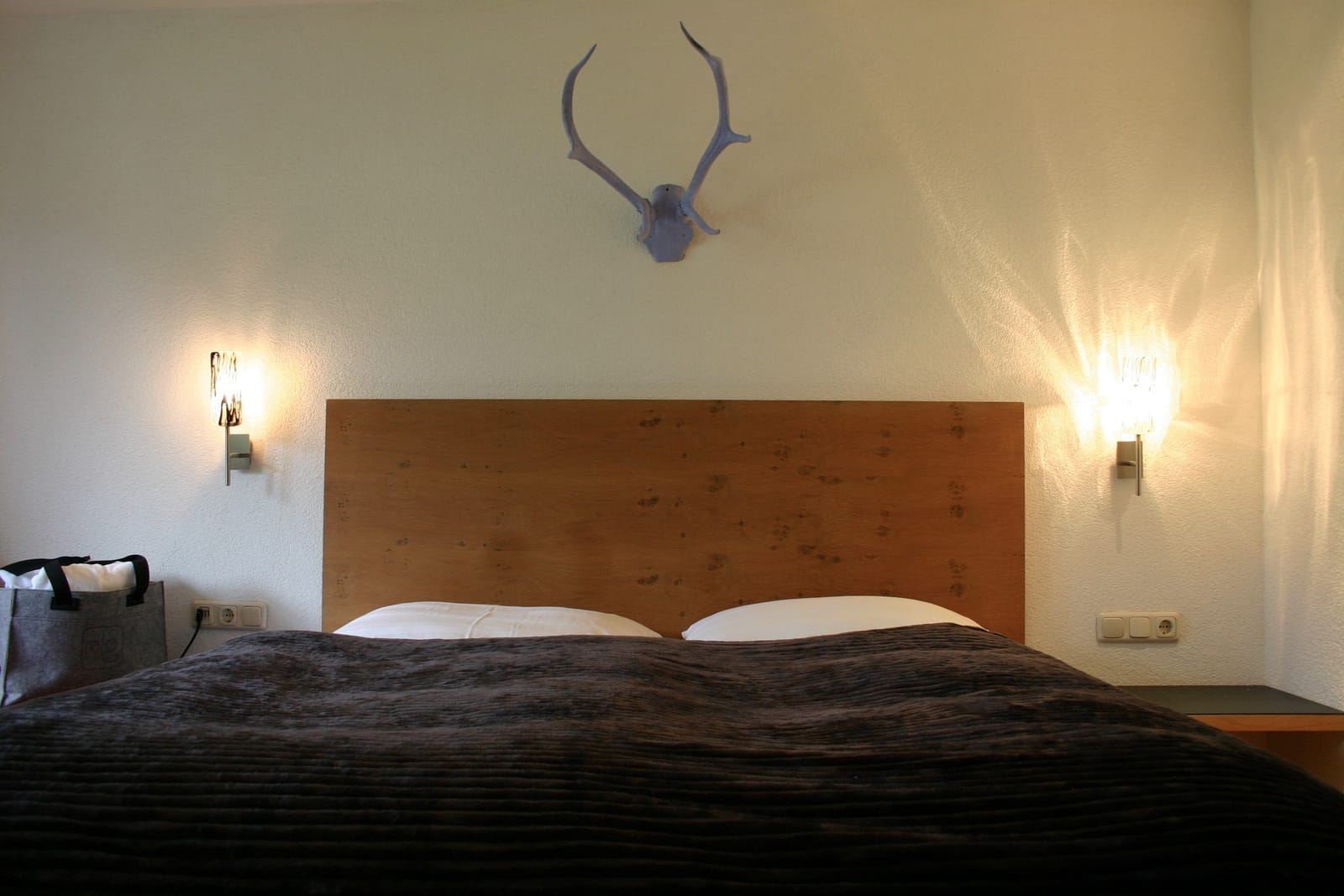 Doppelbett mit Deko-Geweih, Wandleuchten und Holz-Kopfteil – MONTAFONLodge