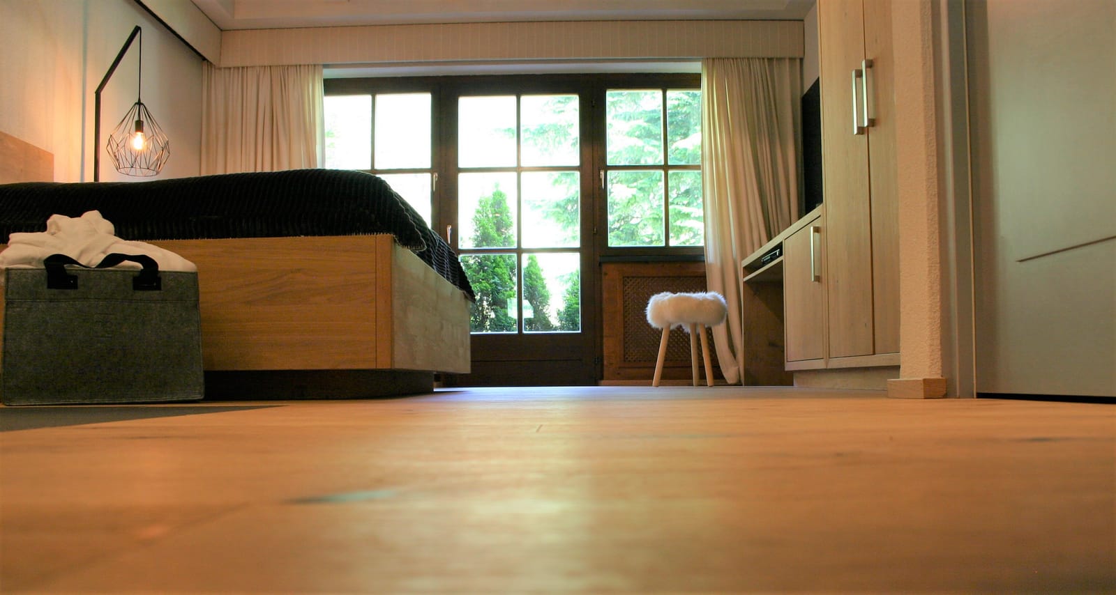 Doppelbett vor Fenster mit Schaffell-Hocker auf Holzboden – MONTAFONLodge